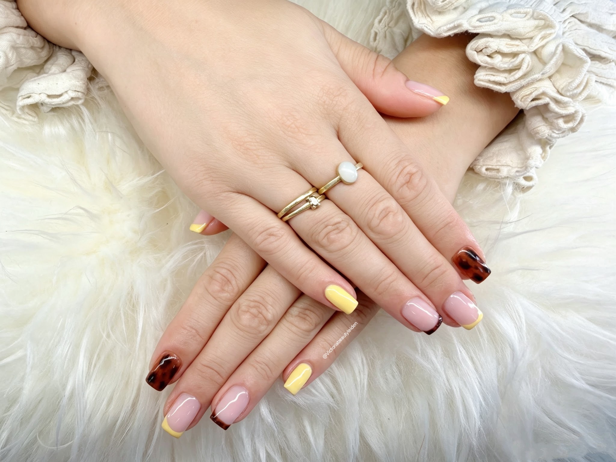 Handen op wit bont met gele French tips en tortoiseshell nagels