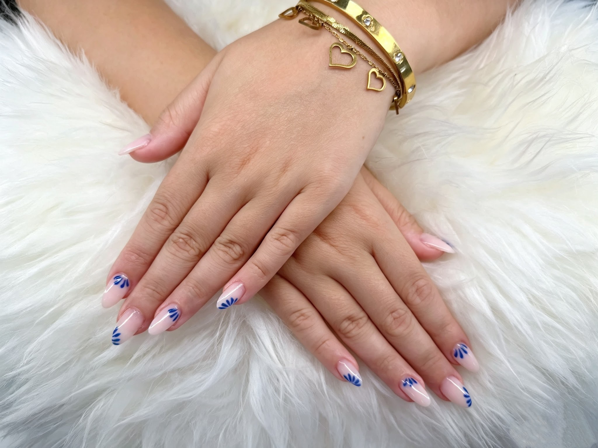 Lichte nagels met blauwe schelp nail art en gouden armbanden op wit bont
