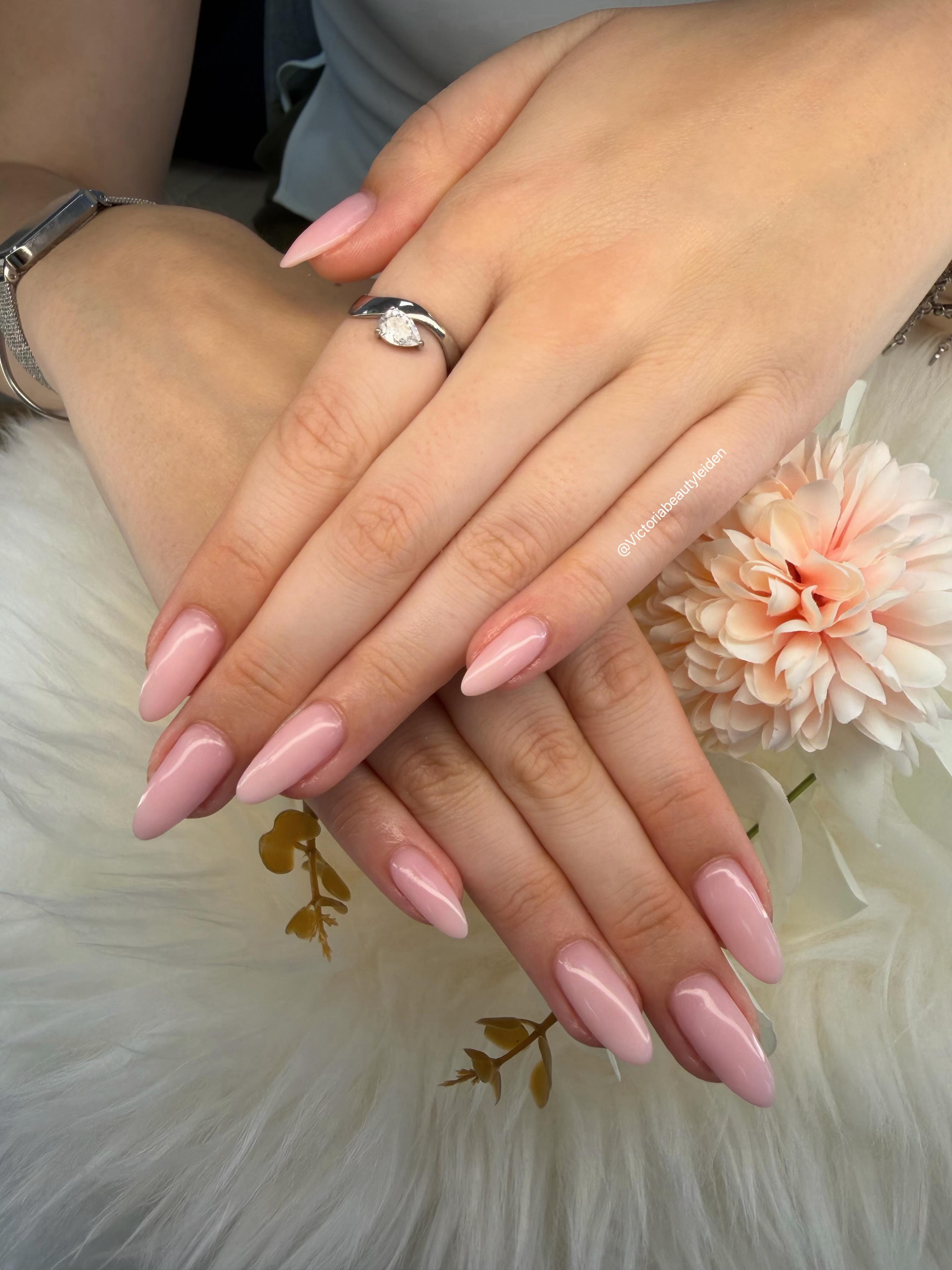 Nude roze amandelnagels naast een perzikkleurige bloem op wit bont